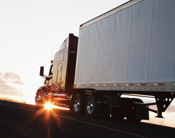 Silhouette of a commercial truck driving on a highway at sunset.